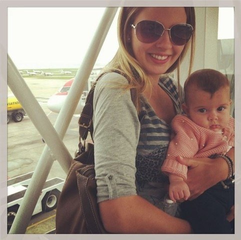Debby Lagranha sorri para foto com filha no colo em aeroporto